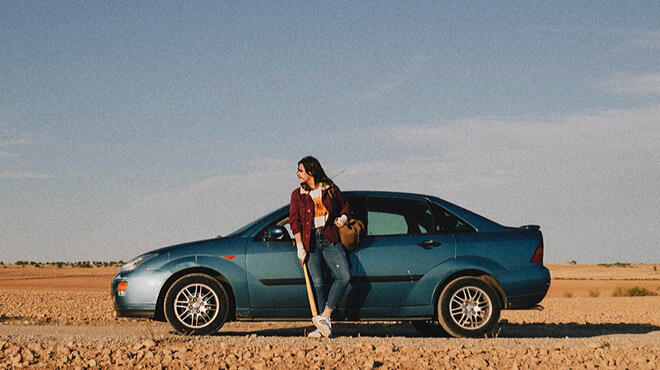 Foto promocional de Ariadna y las Posibilidades Muertas, con Paula apoyada en un coche azul y un bate en las manos.